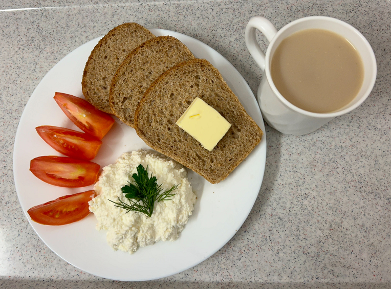 Na zdjęciu znajduje się: Kawa  z mlekiem/p b/c, Chleb graham, Masło extra 82%, Twarożek, Pomidor